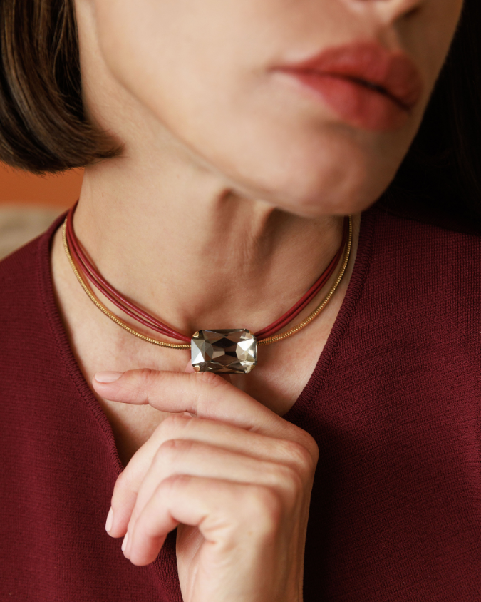 Close-up of a person wearing a necklace with a prominent gemstone, set against a blurred background.