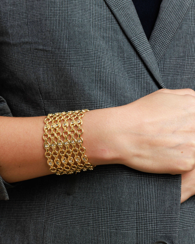 Gold chain bracelet on a wrist with a gray blazer background