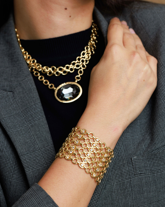 Gold chain necklace and bracelet on a woman wearing a gray blazer.