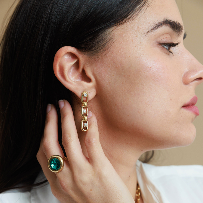 Close-up of a woman wearing gold earrings with a green gemstone.
