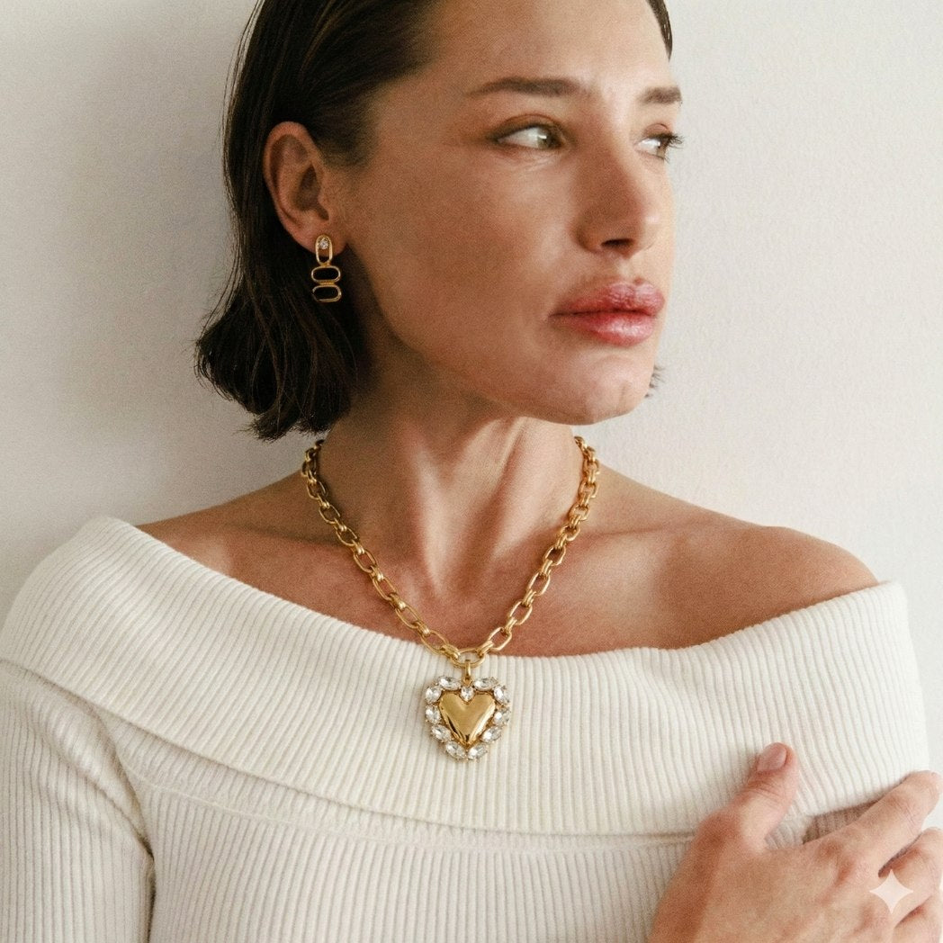 Woman wearing a gold chain necklace with a heart pendant on a plain background