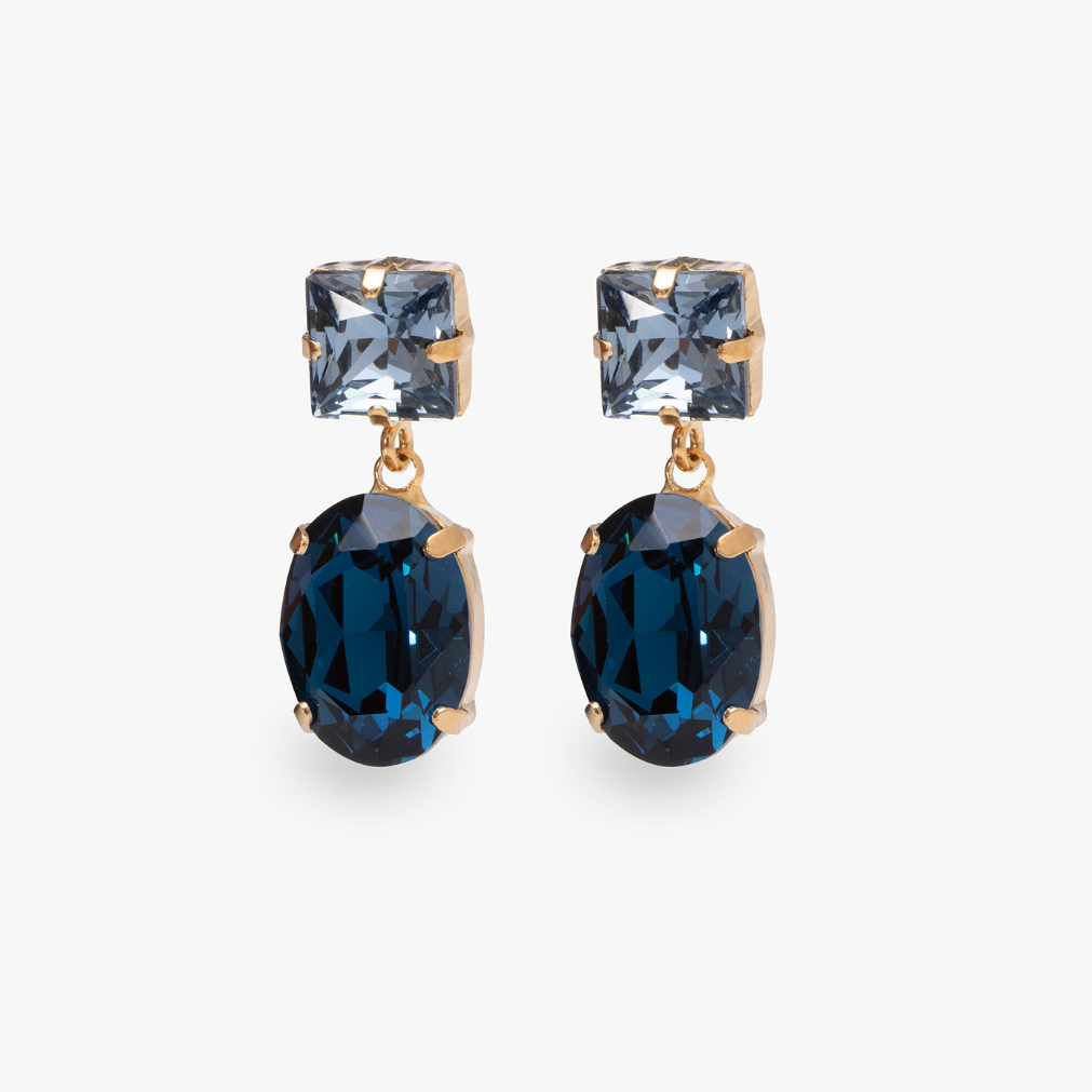 The Oval Glow Earrings, gold-tone earrings with an oval faceted stone, on a light gray background.