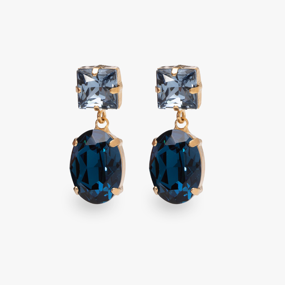 The Oval Glow Earrings, gold-tone earrings with an oval faceted stone, on a light gray background.