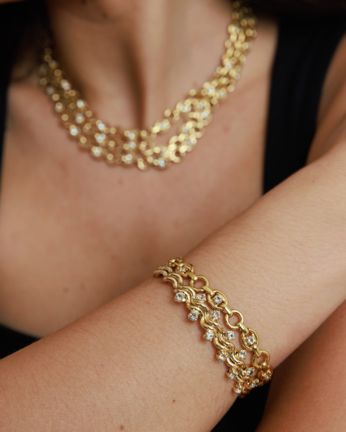 Gold bracelet and necklace on a person against a dark background