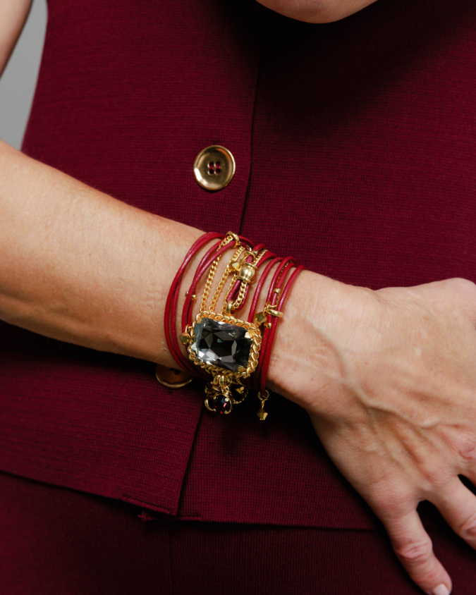 Close-up of a person wearing a gold bracelet with a black stone on a burgundy background