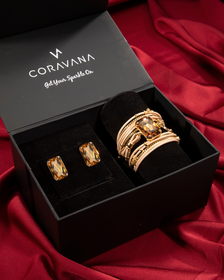 Gold jewelry set including rings and earrings in a Coravana box on a red fabric background