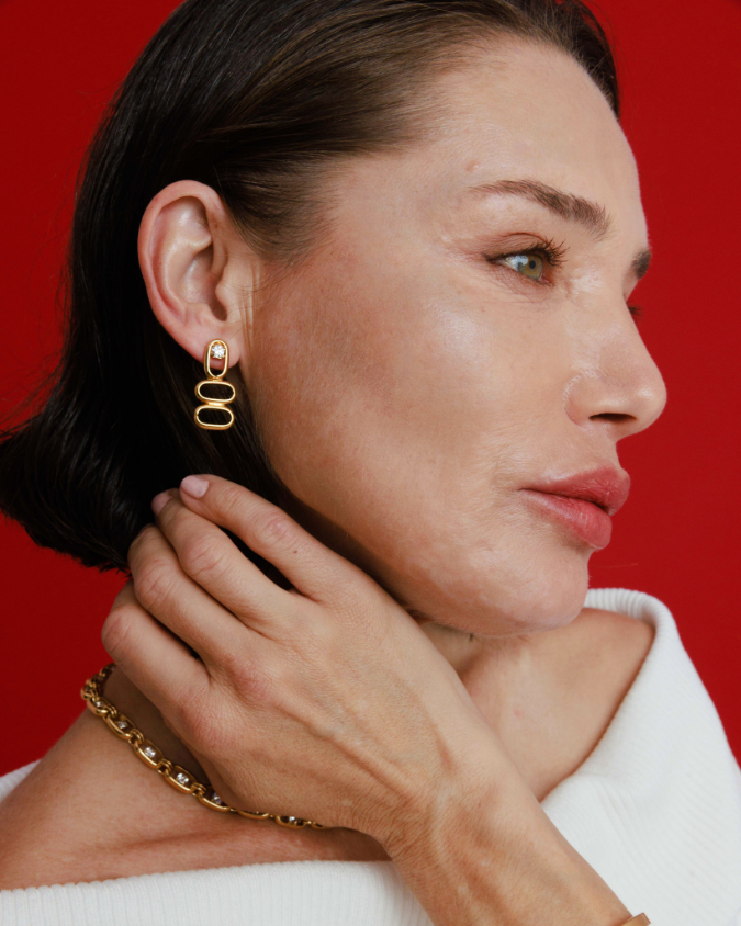 Woman wearing gold earrings and bracelet against a red background