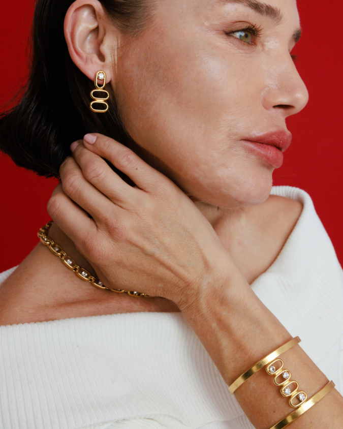 Woman wearing gold earrings and bracelet against a red background
