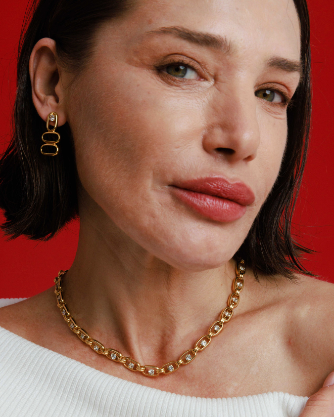 Woman wearing gold earrings and necklace against a red background