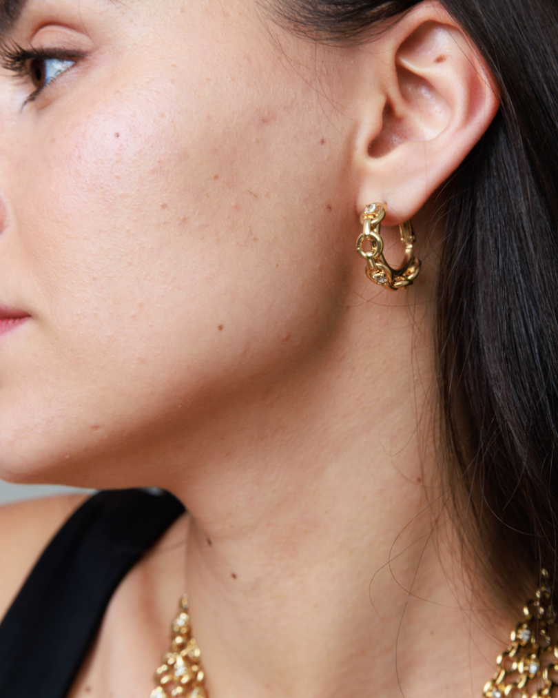 Close-up of a person wearing gold hoop earrings with a blurred background