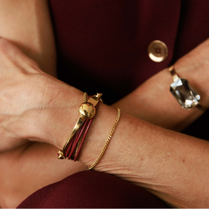 Close-up of a wrist wearing a gold bracelet and ring with a blurred background