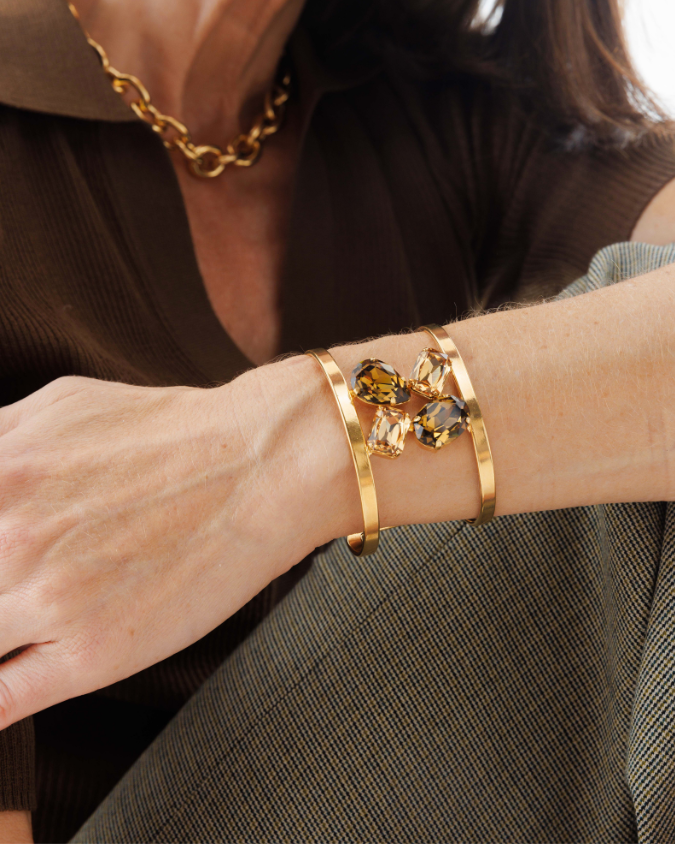 Gold bracelet with gemstones on a wrist against a neutral background