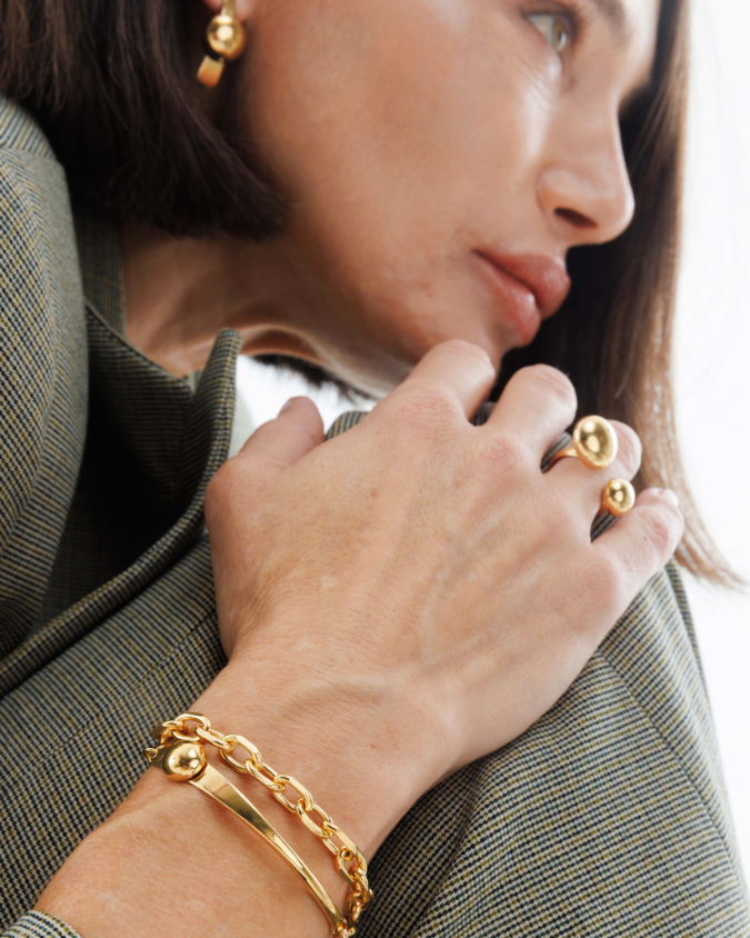 Close-up of a person wearing gold jewelry including earrings, ring, and bracelet.