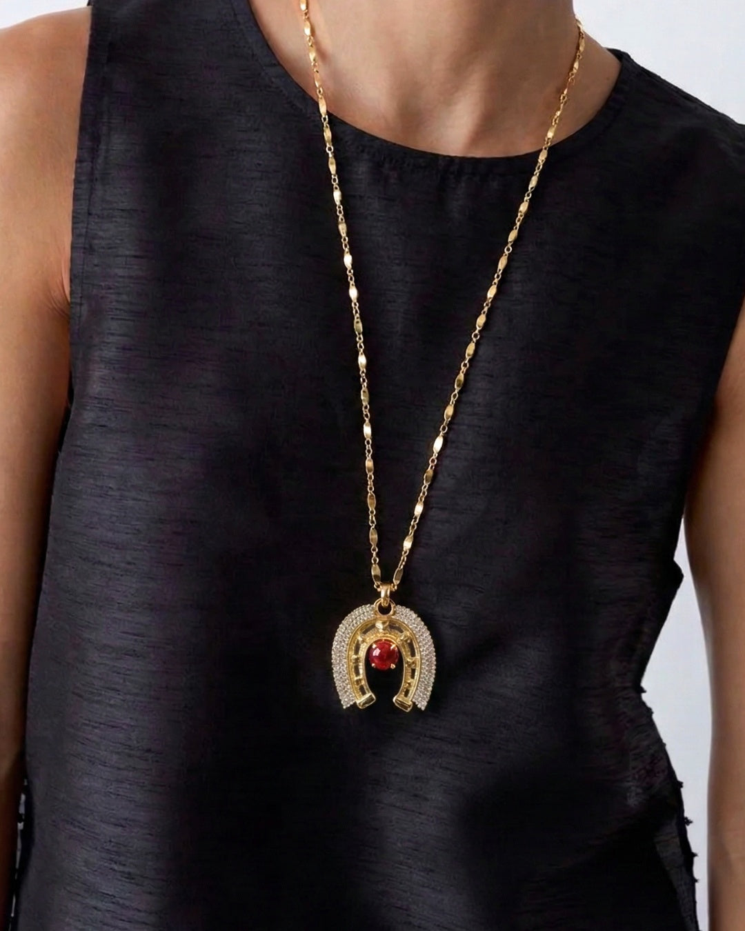 Gold necklace with a red pendant on a black sleeveless top against a white background