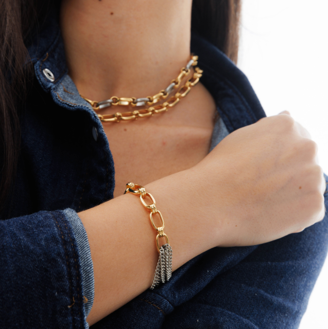 Gold chain bracelet on a person wearing a dark blue denim jacket.