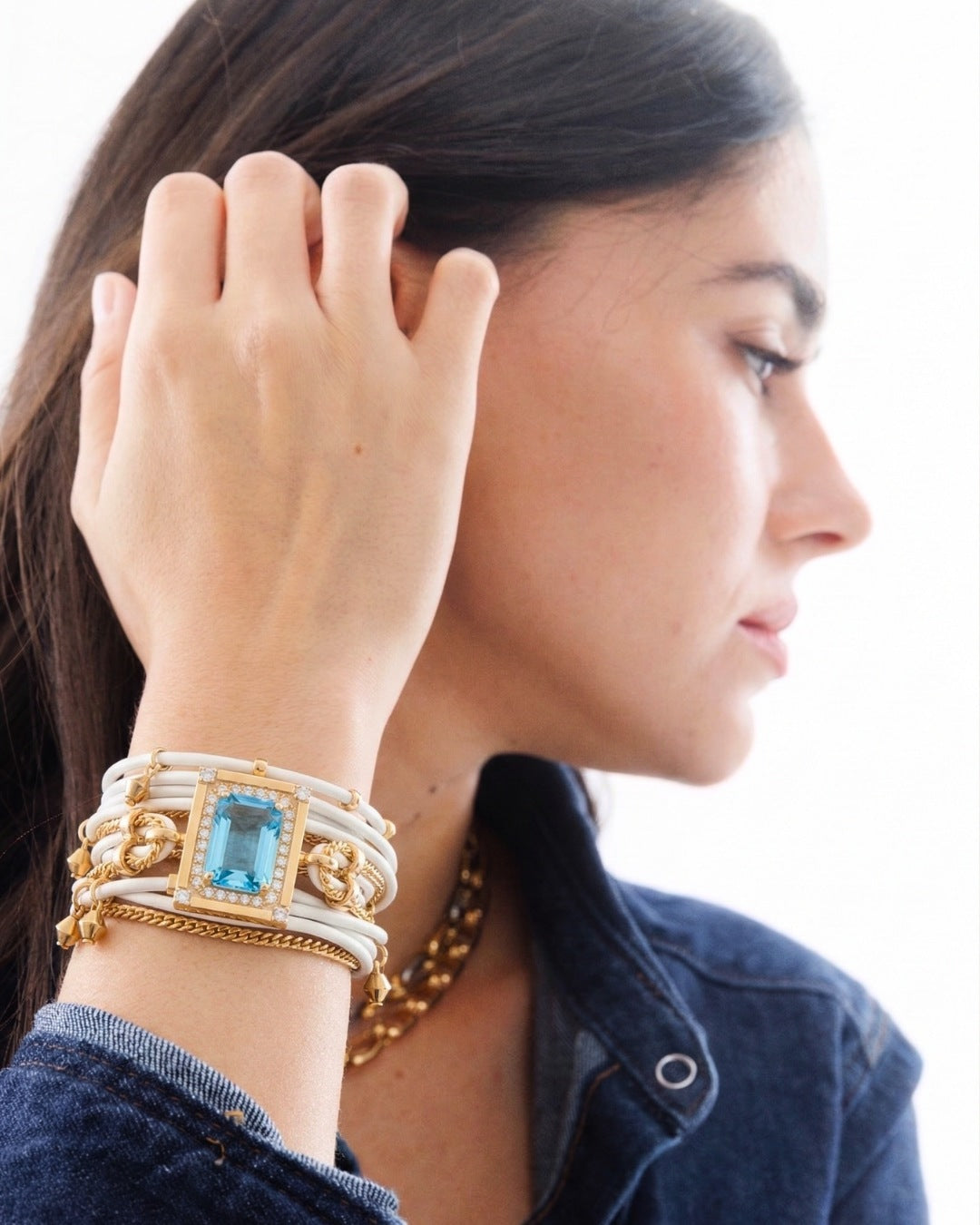 Woman wearing multiple bracelets with a blue gemstone on a plain background