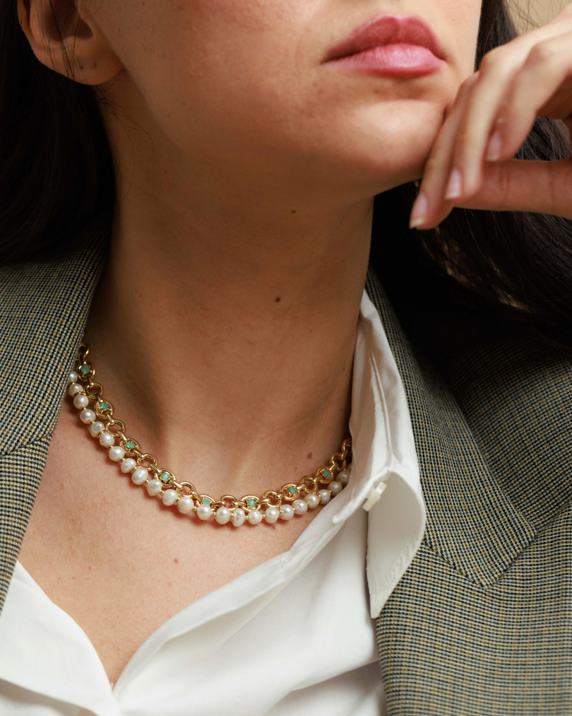 Close-up of a person wearing a pearl necklace with a white shirt and brown blazer.
