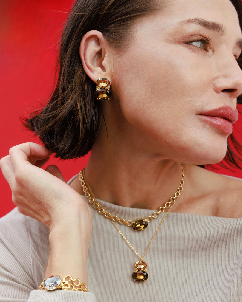 Woman wearing gold jewelry including earrings and a necklace against a red background