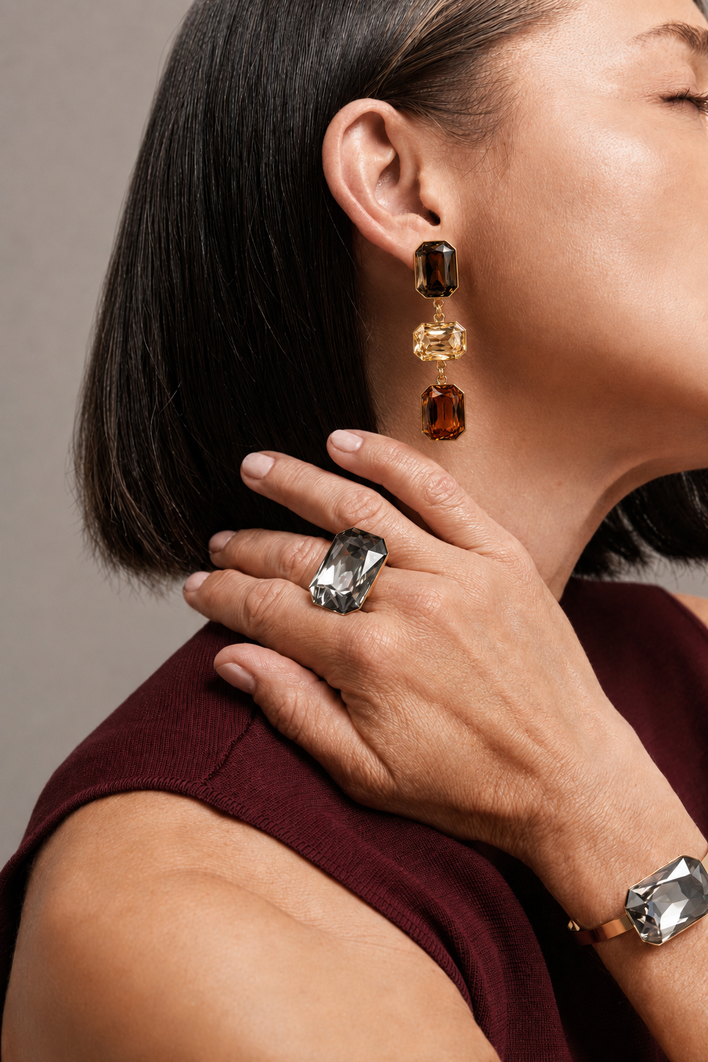 Close-up of a woman wearing a pair of dangling earrings and a ring on a neutral background