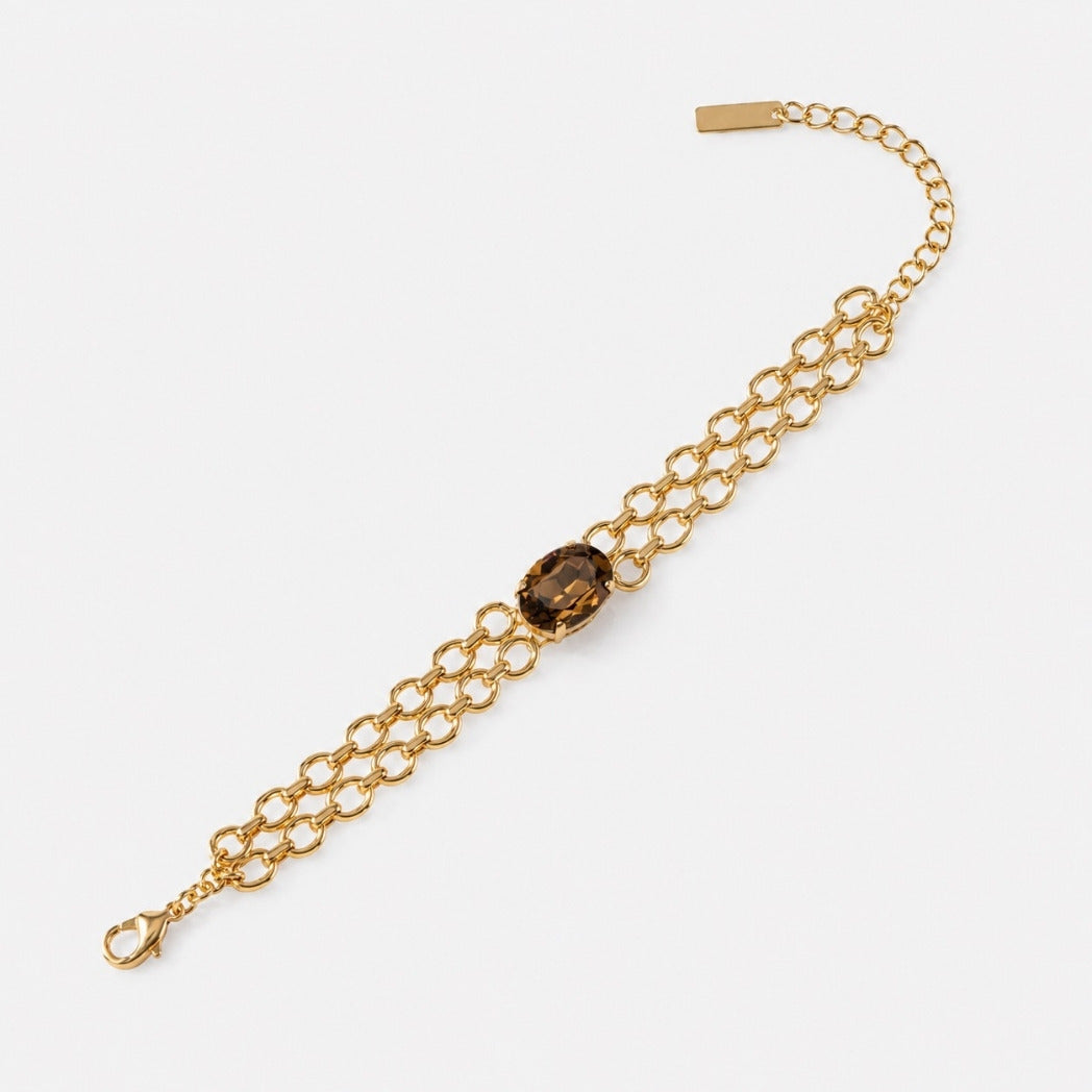 A gold chain bracelet featuring a central oval brown smoky quartz gemstone, displayed on a clean light gray background.