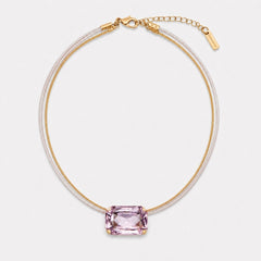 A delicate gold chain necklace featuring a central rectangular pink gemstone pendant, displayed on a clean light gray background.