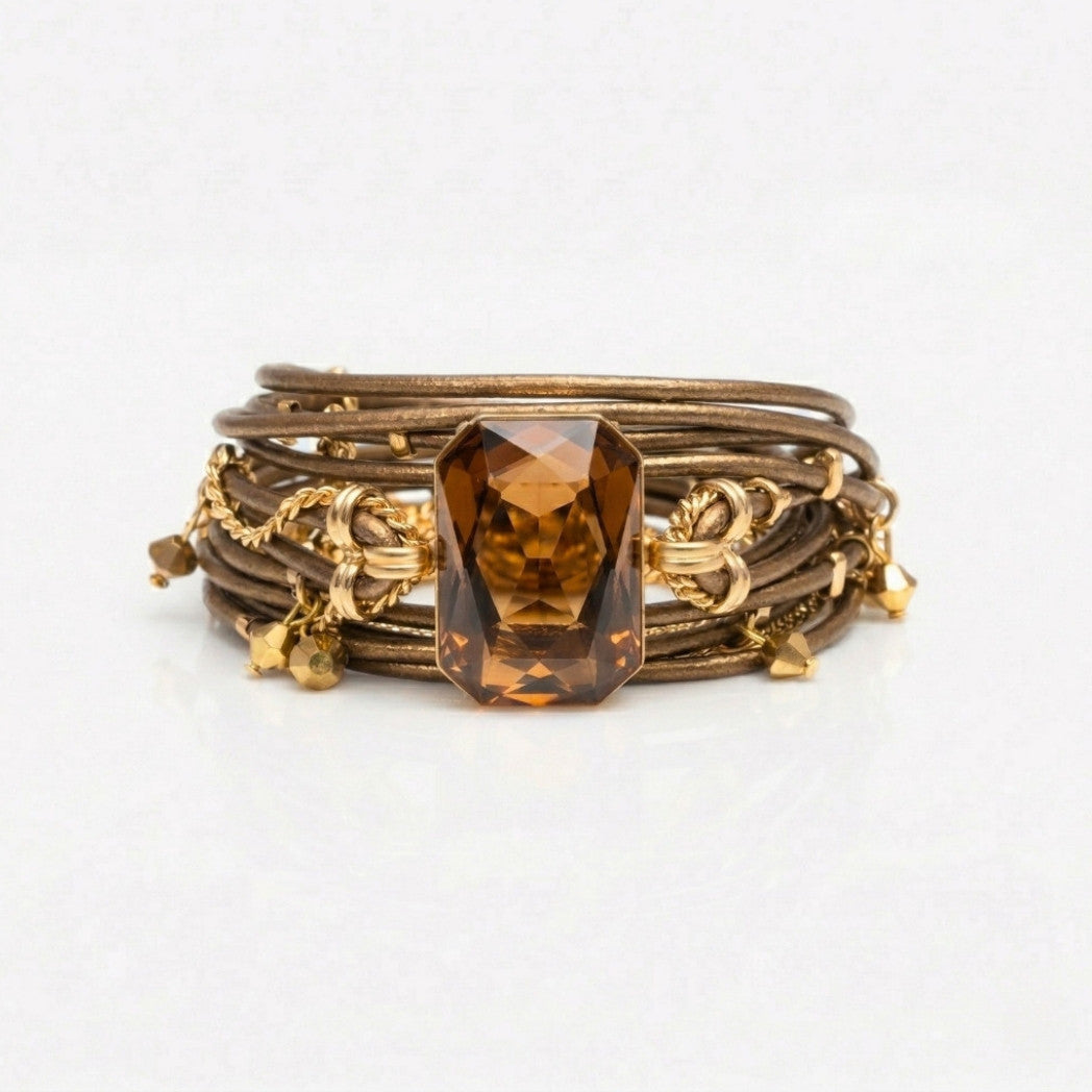 A multi-strand wrap bracelet featuring multiple brown leather bands, gold-toned chain links, small gold charms, and a large faceted brown gemstone centerpiece, set against a plain white background.