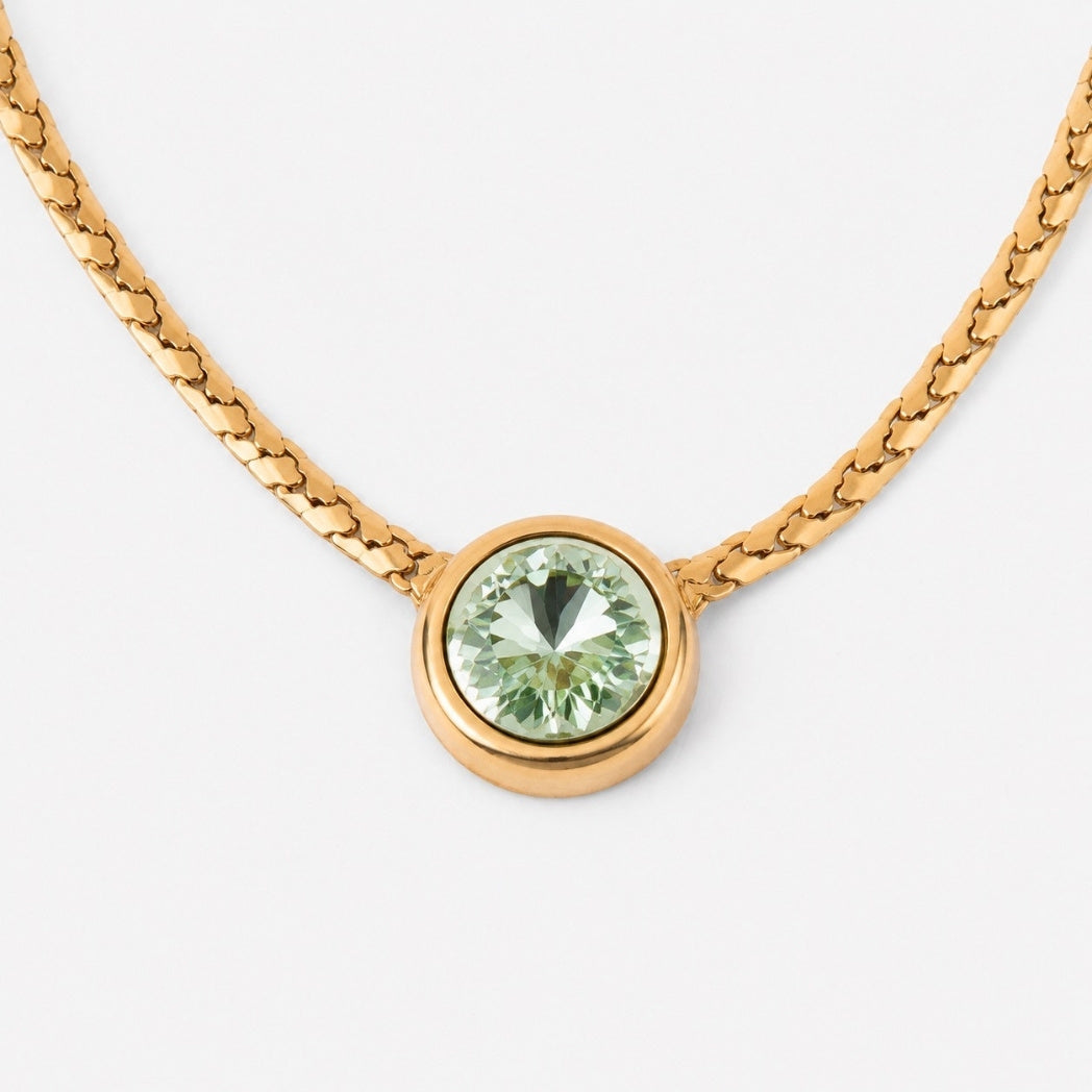 A gold chain necklace featuring a round bezel-set light green gemstone pendant on a clean white background.