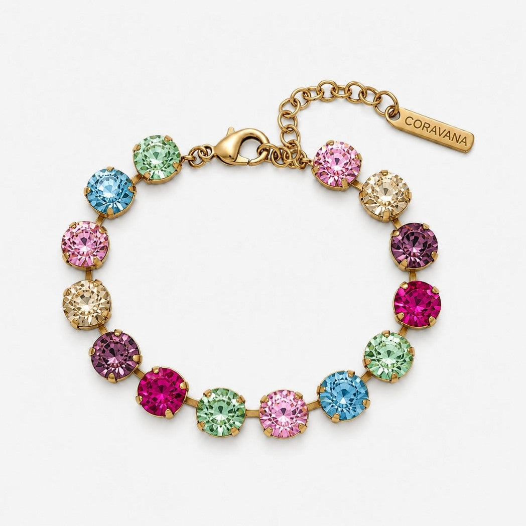 A gold-tone bracelet with round, colorful gemstones in pink, blue, green, and purple, featuring a lobster clasp, extension chain, and a branded tag that reads CORAVANA.