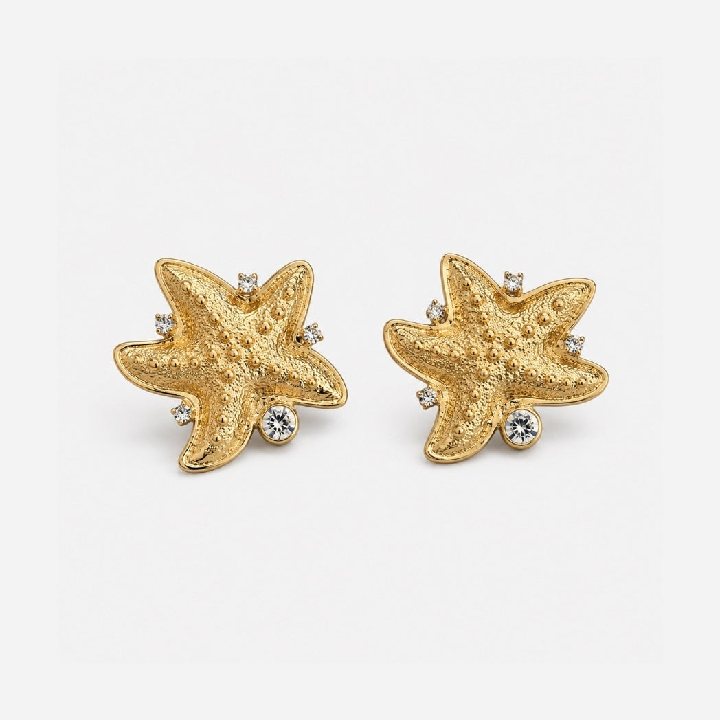 Gold starfish-shaped earrings with embedded crystals on a white background