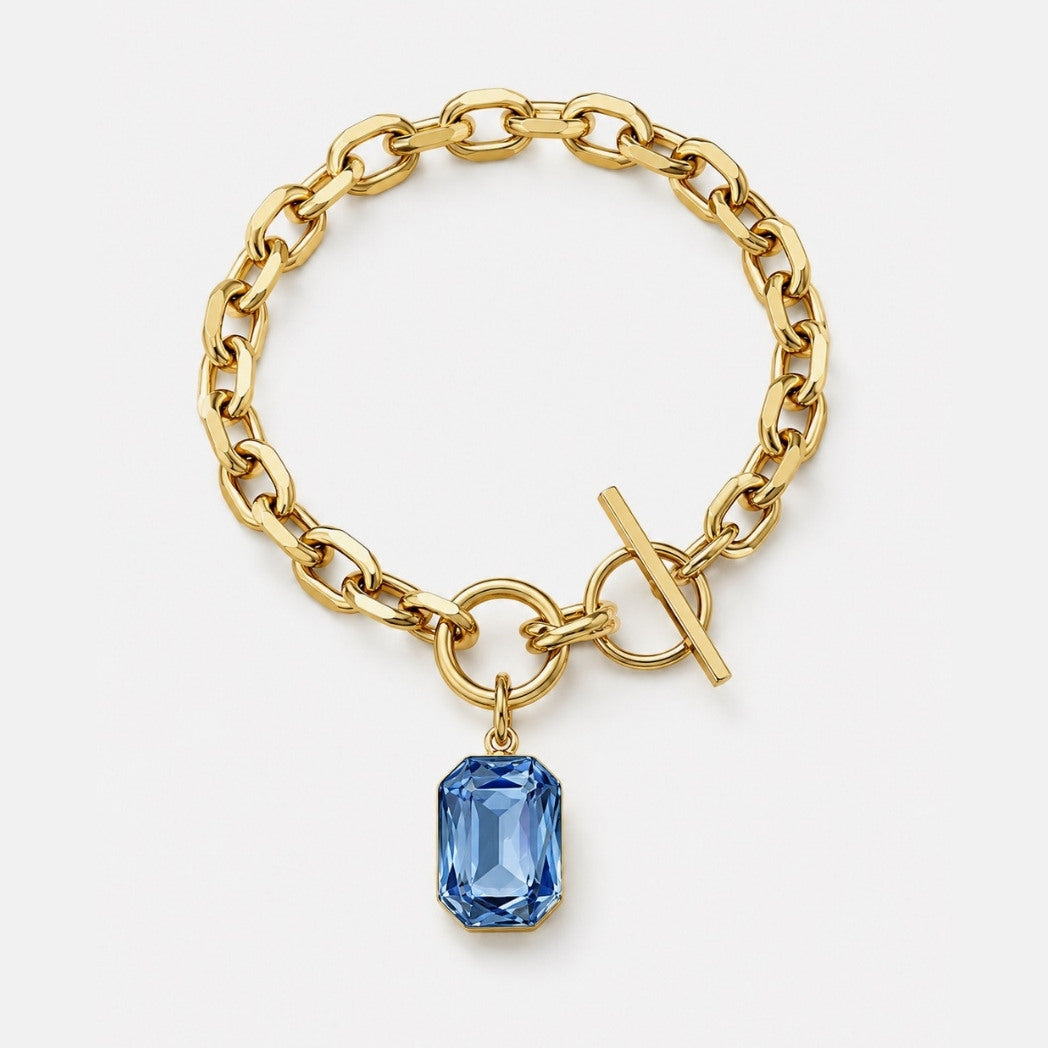 Gold chain bracelet with a blue gemstone charm on a white background