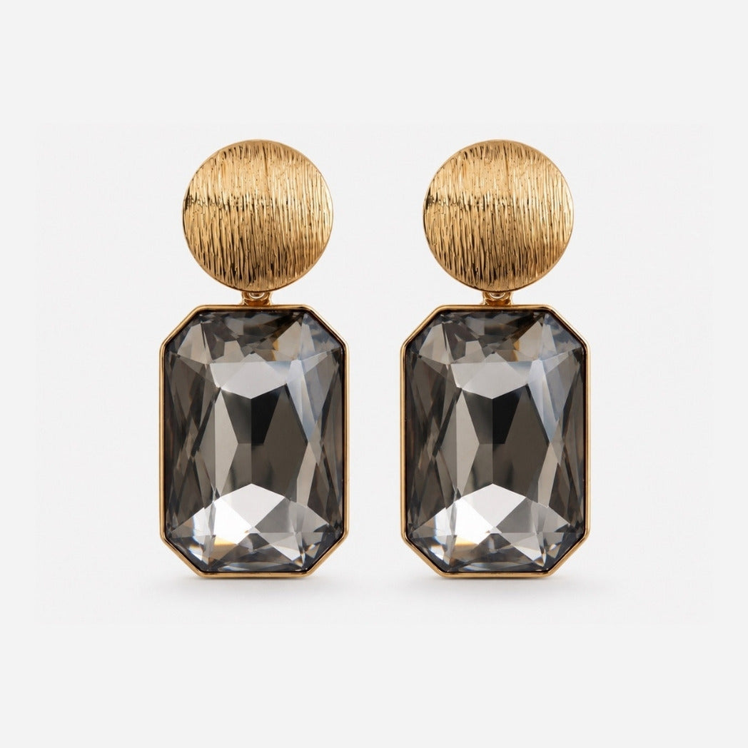 A pair of gold drop earrings featuring a textured round gold top and a large, faceted dark gray rectangular gemstone below, set against a light gray background.