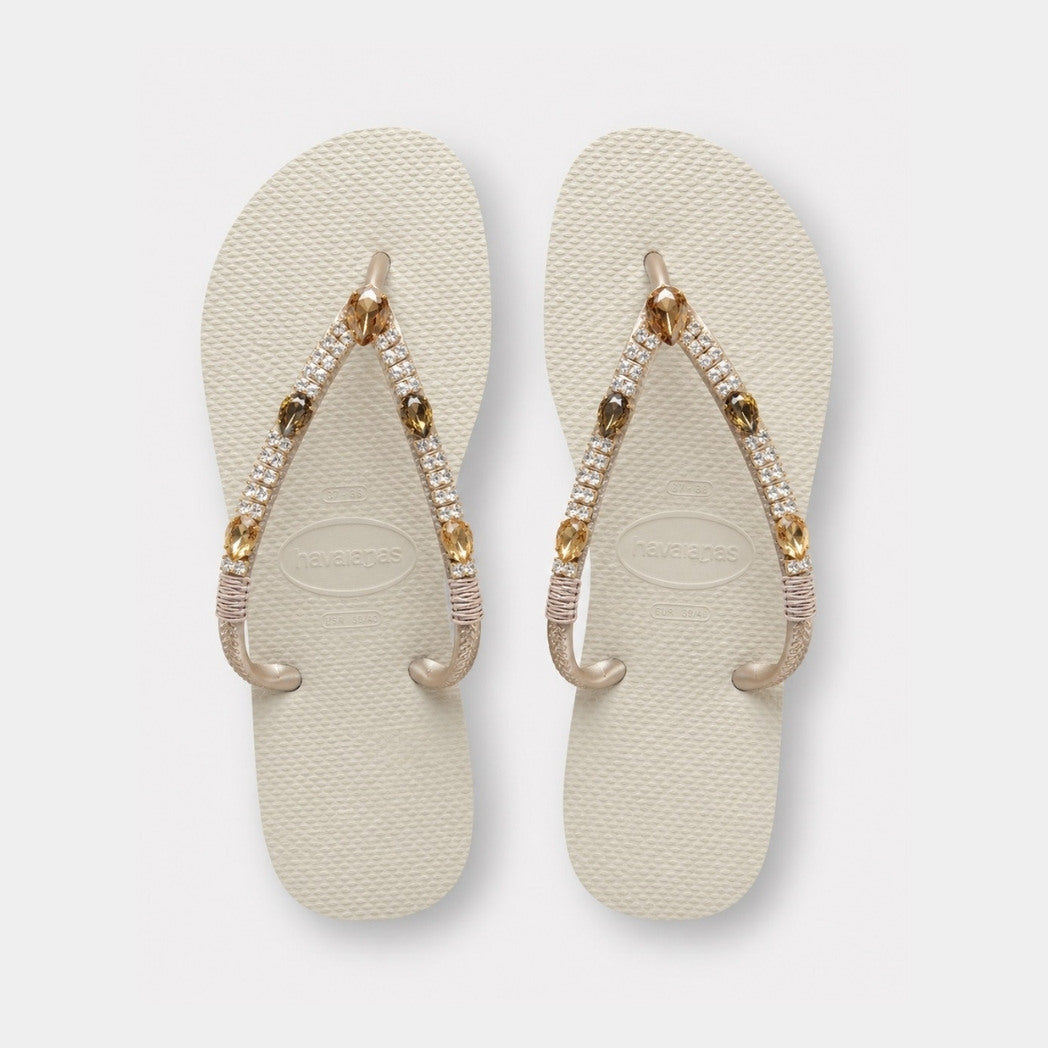 Pair of beige flip-flops with decorative straps on a light gray background
