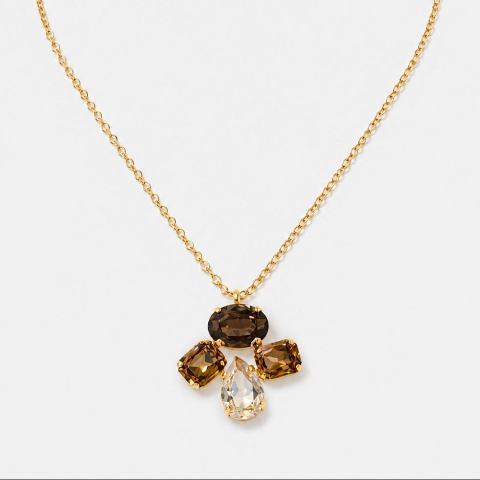 A gold chain necklace with a pendant featuring four gemstones in a flower-like arrangement, including a clear teardrop-shaped stone and three smoky brown rectangular stones, on a light gray background.