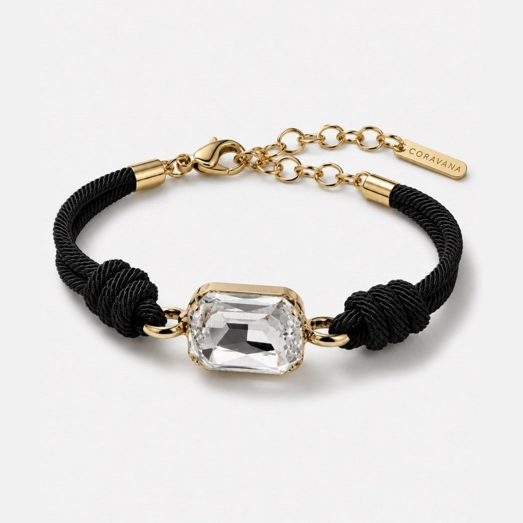 Bracelet with black cord, gold chain, and clear crystal on a white background
