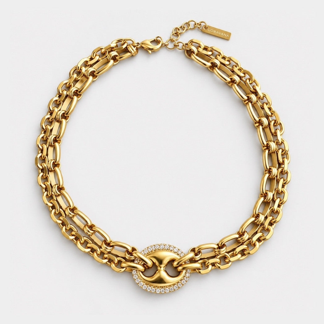 A gold-toned multi-strand chain necklace with a central oval link centerpiece surrounded by small clear stones, photographed on a clean white background.
