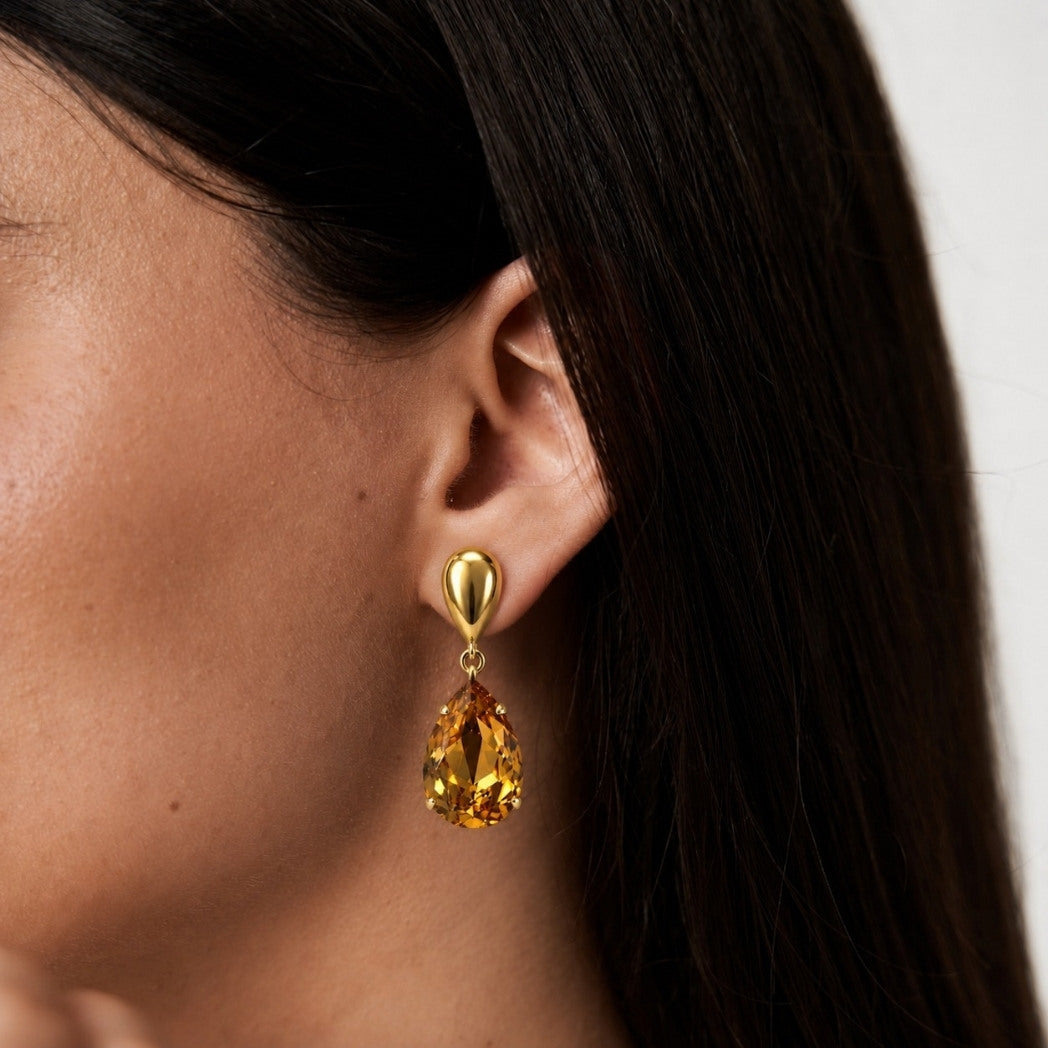 Close-up of a woman's ear wearing a gold earring with a yellow gemstone.