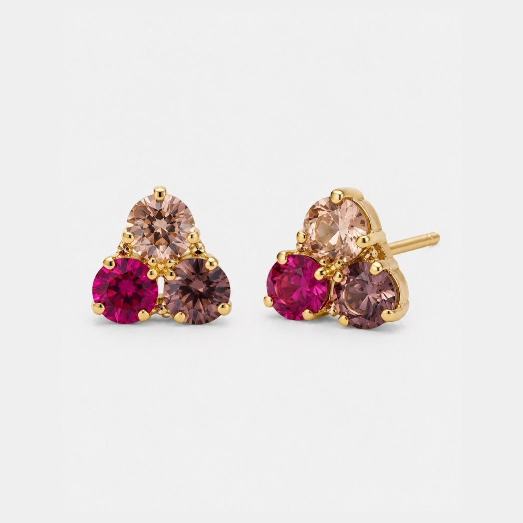 A pair of gold stud earrings featuring a triangular cluster of three marquise-cut champagne-colored stones and two round-cut bright pink gemstones, shown on a light gray background.
