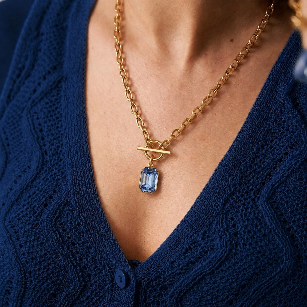 Gold necklace with a blue pendant worn by a person in a blue textured garment.