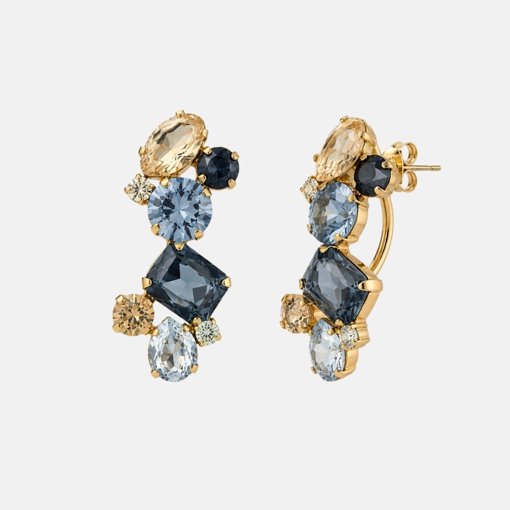 A pair of gold drop earrings featuring a cluster of faceted gemstones in light blue, dark blue, pale yellow, and clear shapes on a light gray background.
