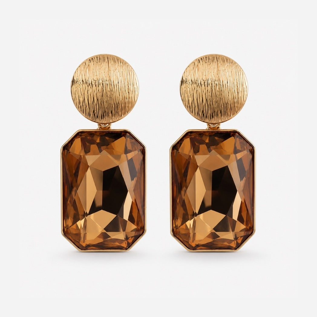 A pair of gold drop earrings featuring a round textured gold top and a faceted rectangular brown gemstone drop, shown on a light gray background.