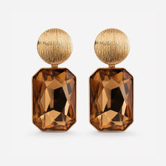 A pair of gold drop earrings featuring a round textured gold top and a faceted rectangular brown gemstone drop, shown on a light gray background.