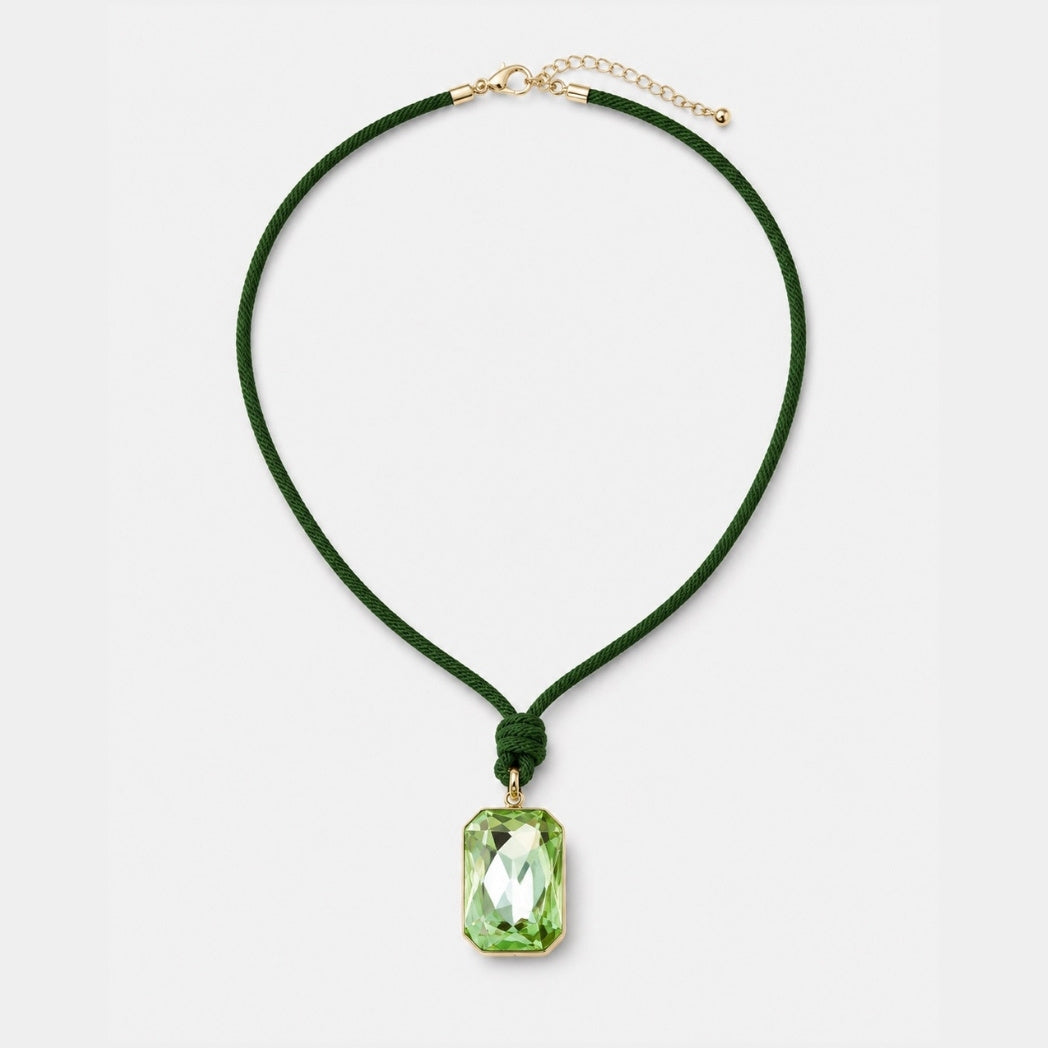 A dark green cord necklace with a faceted green rectangular pendant and gold-tone hardware, displayed on a clean light gray background.