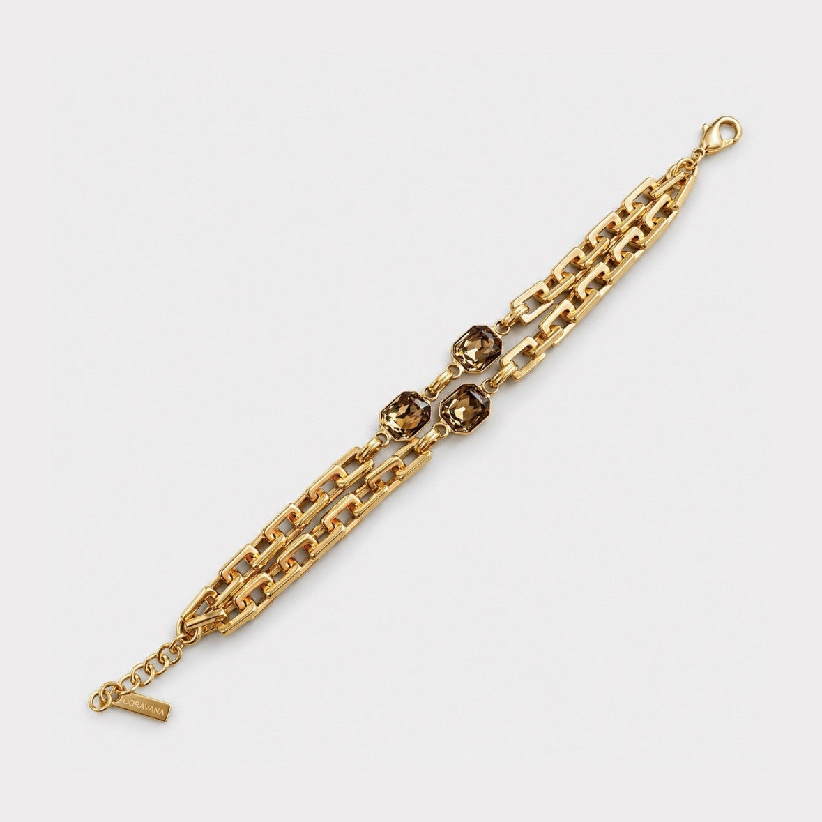 A gold-toned chain bracelet featuring three central smoky brown faceted gemstones, displayed on a clean light gray background.