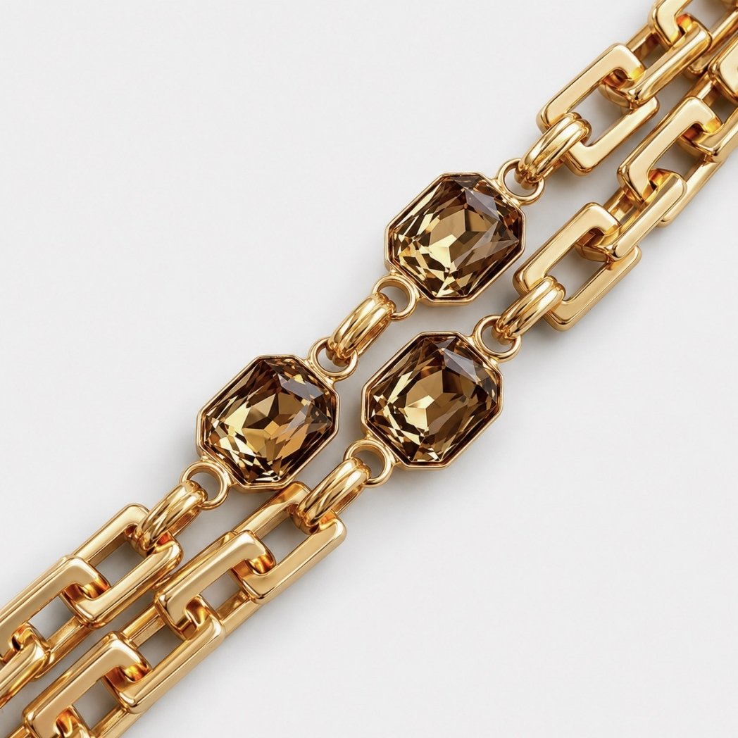 A close-up of a gold-toned chain bracelet featuring three faceted brown smoky crystal links, set against a clean light gray background.