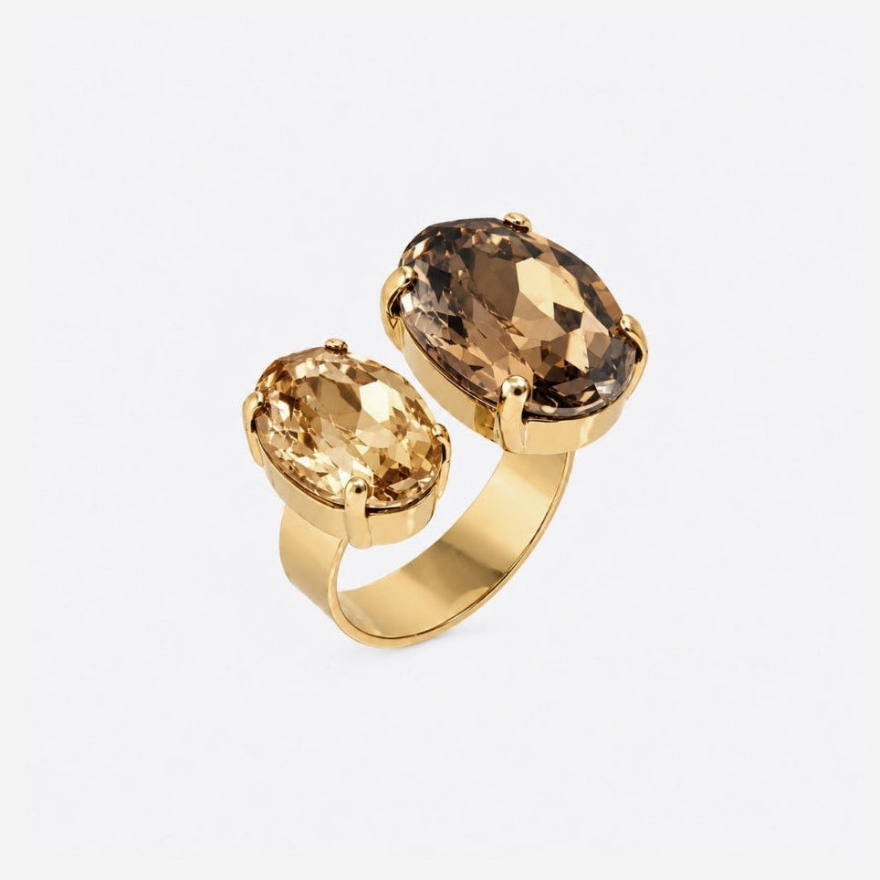A gold ring featuring two oval-cut gemstones, one in a warm champagne yellow and the other in a smoky brown, set on a clean white background.
