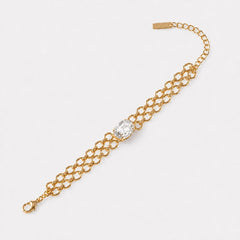 A gold chain bracelet featuring a central bezel-set clear oval gemstone, displayed on a clean white background.