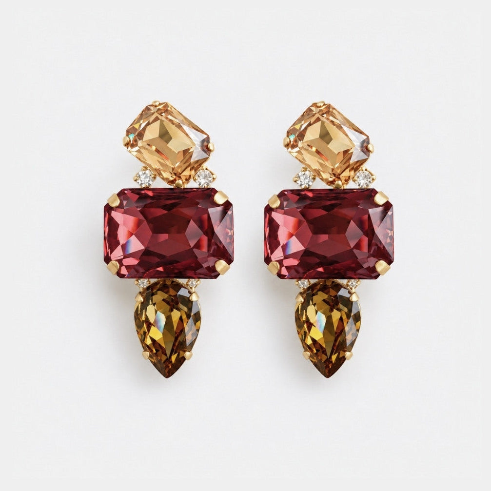 A pair of gold-tone drop earrings featuring a large rectangular burgundy-red gemstone, a smaller champagne-colored gemstone above, and a teardrop-shaped brown gemstone below, set against a plain light gray background.