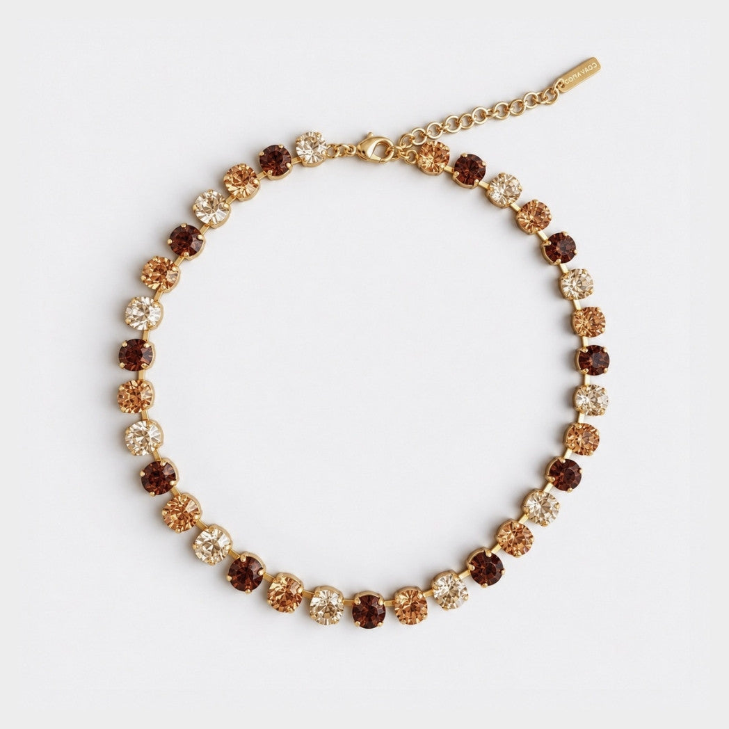 A gold chain bracelet with alternating round brown and champagne-colored crystal rhinestones, displayed on a clean white background.