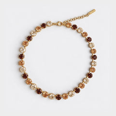 A gold chain bracelet with alternating round brown and champagne-colored crystal rhinestones, displayed on a clean white background.