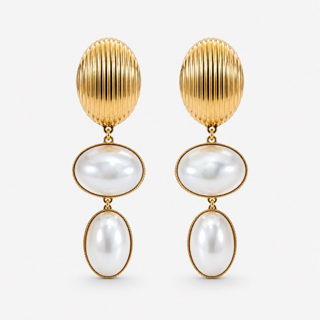 A pair of gold drop earrings featuring a vertically ribbed oval top, a horizontal oval pearl drop, and a smaller vertical oval pearl drop, set against a light gray background.